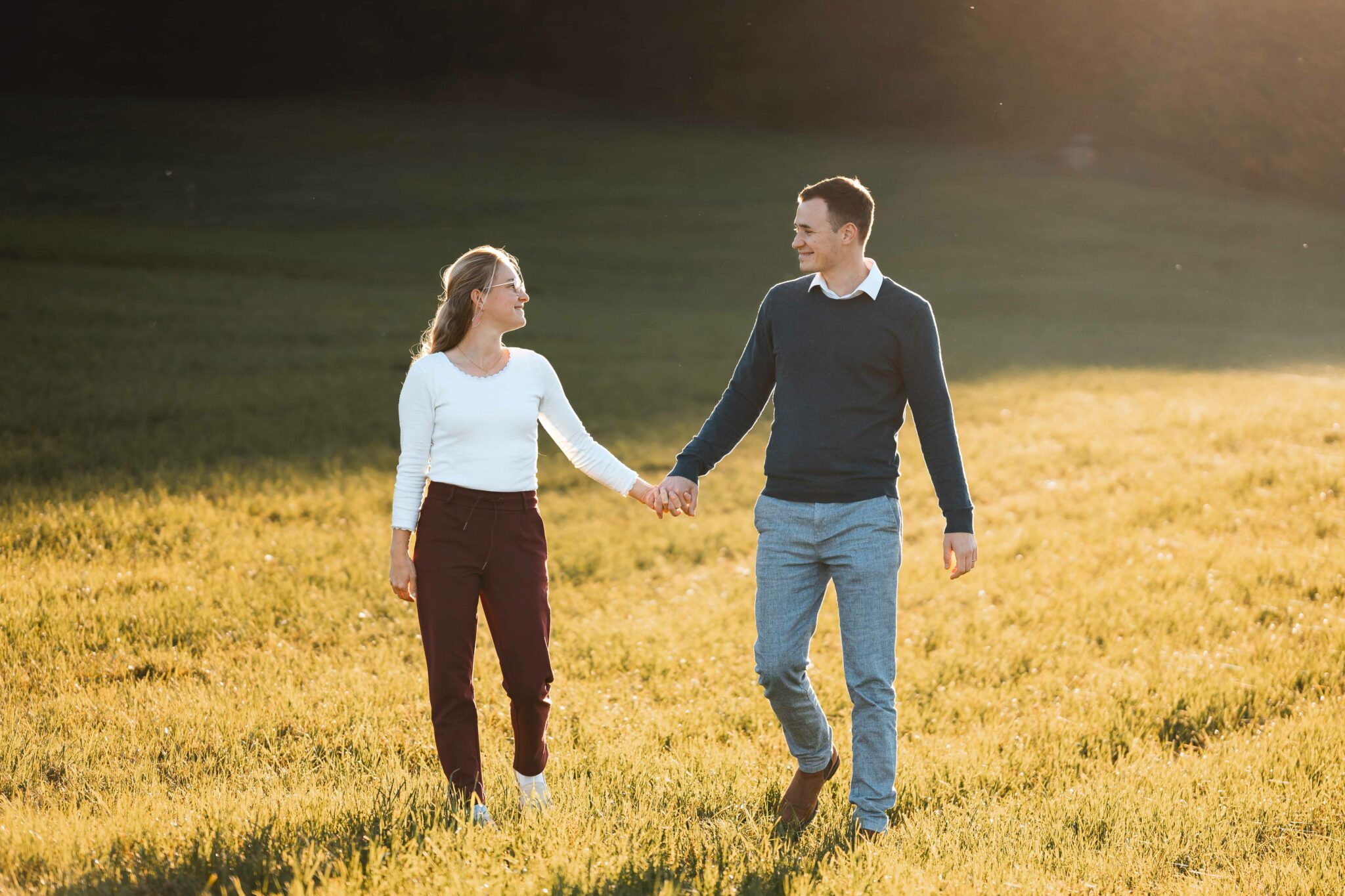 Fotografenpaar läuft auf einer Wiese im Sonnenuntergang und hält sich die Hände
